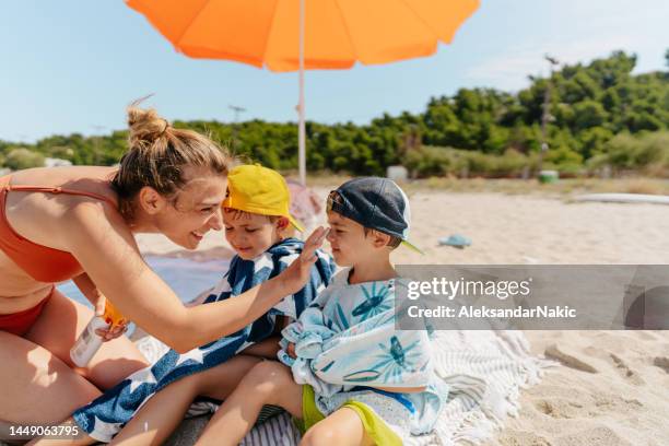 mutter trägt sonnencreme auf ihre jungs auf, während sie am strand ist - sonnenschutz stock-fotos und bilder