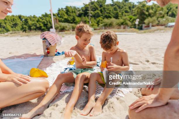 glückliche familie, die sonnencreme am strand aufträgt - suntan lotion stock-fotos und bilder