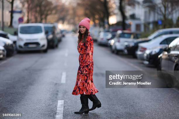 Anna Wolfers seen wearing a red, orange and black patterned long dress, a black belt, black cowboy boots and a pink beanie on December 09, 2022 in...