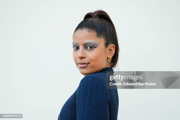 Guest wears gold earrings, a navy blue ribbed long sleeves / long tube dress, outside the "Le Raphia" Jacquemus show on December 12, 2022 in Le...