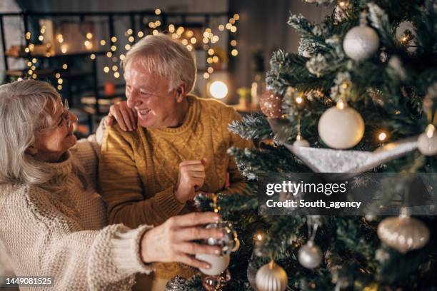 senior couple decorating christmas tree at home - kerstboom versieren stockfoto's en -beelden