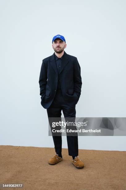 Guest wears a royal blue cap with white embroidered "Style Not Com" slogan, a black shirt, a black oversized blazer jacket, black suit pants, black...