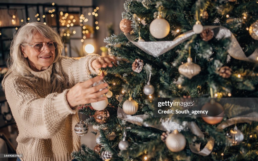 Seniorin schmückt Weihnachtsbaum zu Hause