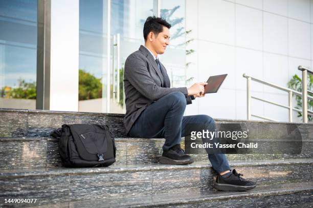 asian businessman using tablet at building entry - borsa messenger foto e immagini stock