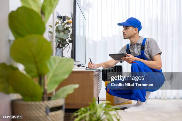 customer service and support for electronic products. an asian male technician service support is setting up a tv set and adjusting the channel tuner during installation in a living room at a customer's home. - retailer shopping customer tv stockfoto's en -beelden