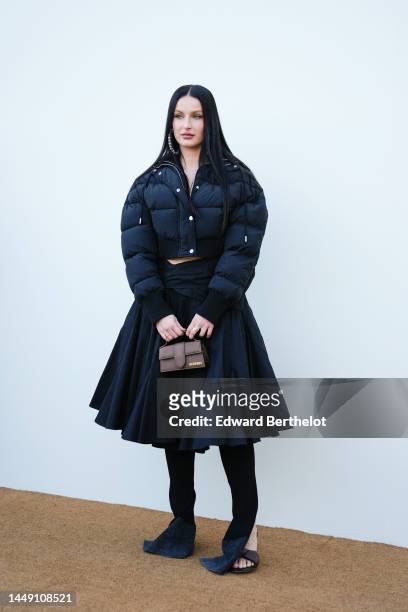Fiona Zanetti wears silver large pendant earrings, a black cropped puffer jacket, rings, a brown shiny leather handbag from Jacquemus, a black high...