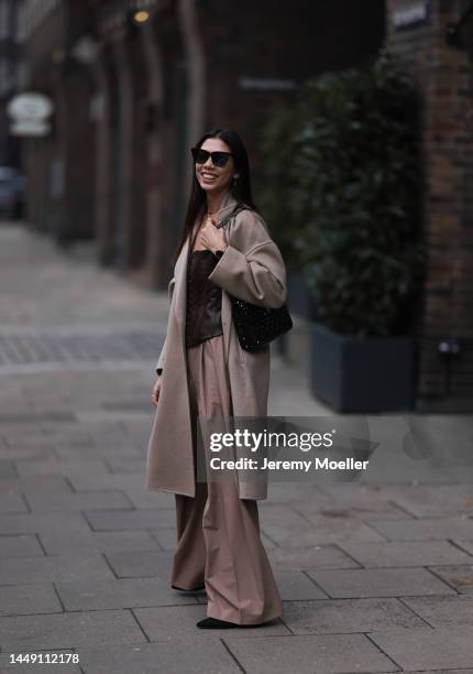 Mira Mintz seen wearing beige long wool coat, brown sunglasses, dark brown leather top, silver necklace and earrings, beige wide leg suit pants,...