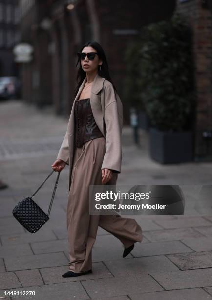 Mira Mintz seen wearing beige long wool coat, brown sunglasses, dark brown leather top, silver necklace and earrings, beige wide leg suit pants,...