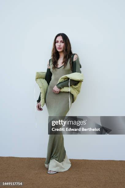 Guest wears a khaki V-neck / long sleeves / cut-out shoulder / long wool tube dress, a pale green sleeveless puffer jacket, outside the "Le Raphia"...