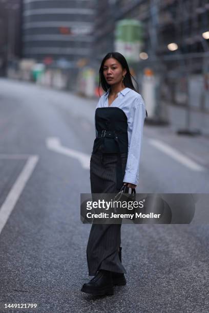 Lan Anh Ho seen wearing silver earrings, light blue button shirt, black corset top, black striped long skirt, black leather bag and black leather...