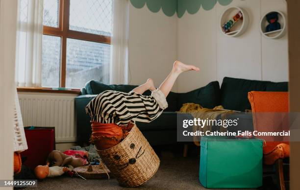 a child suffers a minor, humorous fall as she messes about in a wicker basket. the basket over balances with her upside-down inside it. - birichinata foto e immagini stock