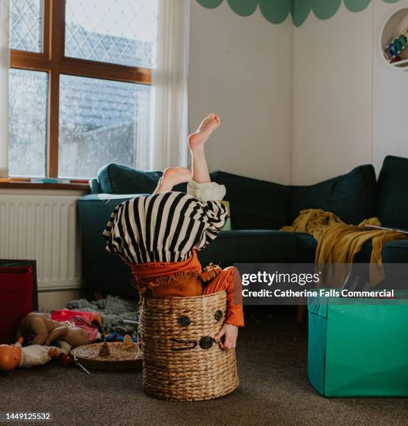 a child suffers a minor, humorous fall as she messes about in a wicker basket. the basket over balances with her upside-down inside it. - zeit verschwenden stock-fotos und bilder