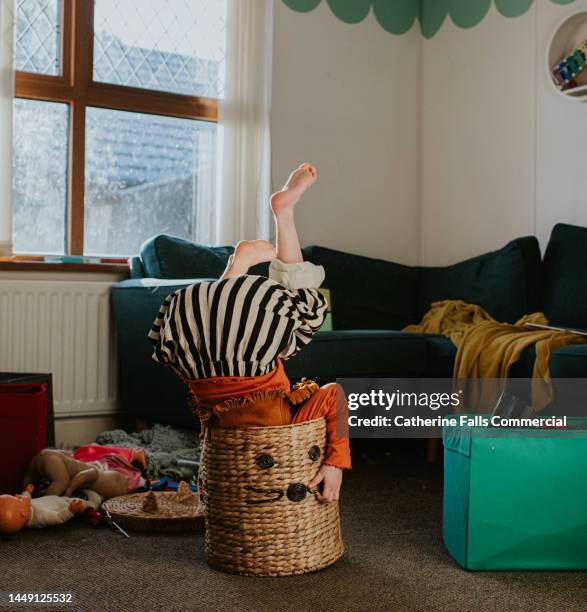 a child suffers a minor, humorous fall as she messes about in a wicker basket. the basket over balances with her upside-down inside it. - lantern photos et images de collection