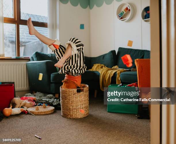 a child suffers a minor, humorous fall as she messes about in a wicker basket. the basket over balances with her upside-down inside it. - stuck inside fotografías e imágenes de stock