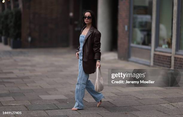 Lorena Katona seen wearing dark brown blazer jacket, black sunglasses, blue denim bandeau top, matching blue denim pants, fluffy white cream shoulder...