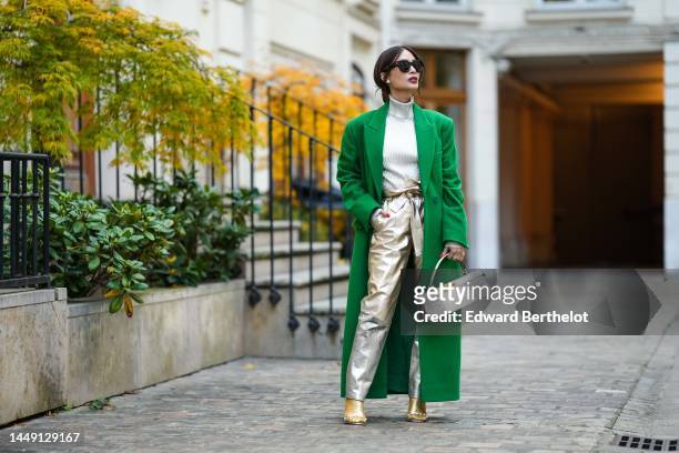 Heart Evangelista wears black sunglasses, gold earrings, a silver varnished ribbed pullover, a green wool long coat, silver shiny leather large...