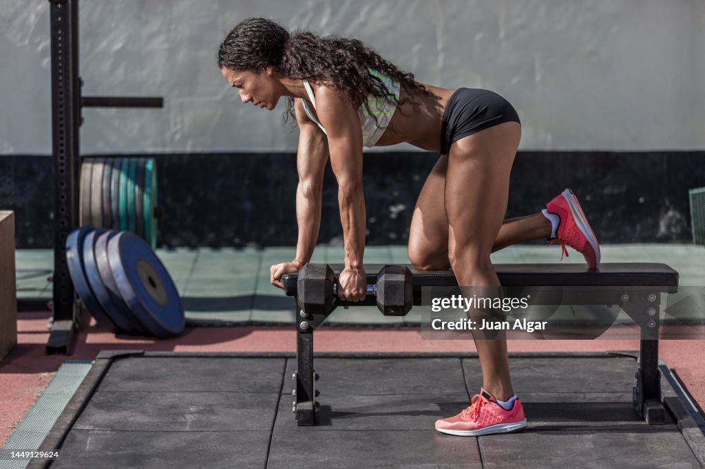 Strong sportswoman exercising with dumbbell on bench