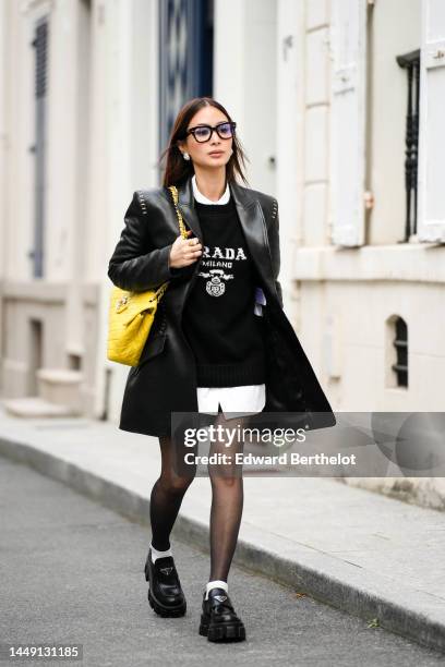 Heart Evangelista wears black glasses, diamonds earrings, a black shiny leather blazer jacket, a yellow shiny leather shoulder bag from Chanel, a...