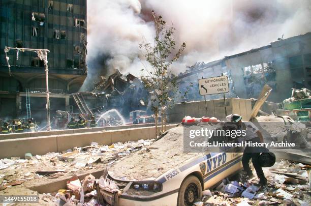 Rescue worker reaching into a New York Police car covered with debris with smoldering ruins in background, Terrorist Attack on World Trade Center,...