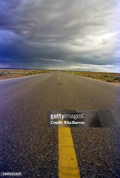 Low-angle view along an empty road in the desert, Arizona, August 2006. Storm clouds are visible in the distance.