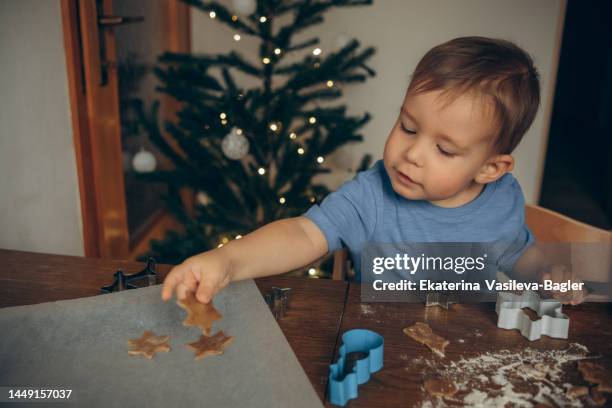 portrait of a child cooking gingerbread christmas cakes with colorful cookie molds  puts it on a baking sheet - wachspapiere stock-fotos und bilder