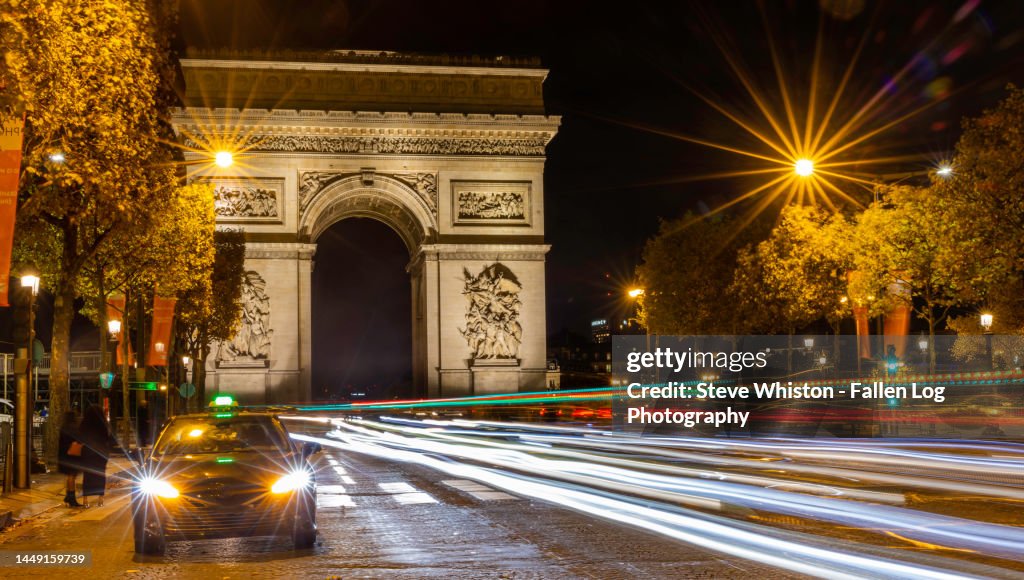 Time Exposure of Heavy Traffic Patterns Along the Avenue des Champs-Élysées Boulevard in Paris at Night with a Taxi Waiting in the Foreground and the Arc de Triomphe in the Background
