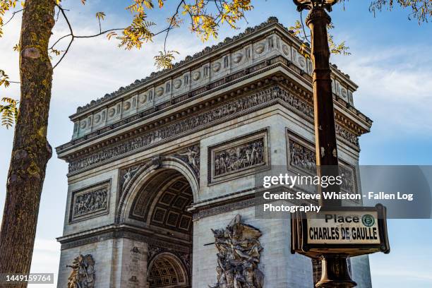 view of arc de triomphe in paris with street sign identifying place charles de gaulle with blue sky, clouds, and fall foliage in trees. - champs elysees stock pictures, royalty-free photos & images