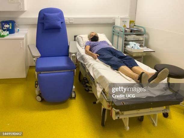 Southern England, UK, Elderly female patient laying on hospital bed in a recovery room after receiving medical treatment.