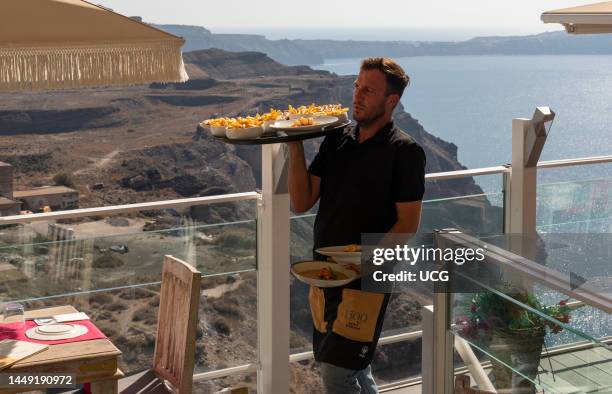 Fira, Santorini, Greece, Waiter carrying food dishes in a clifftop restaurant bistro in Fira, overlooking the Aegean Sea, Santorini.