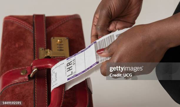 Bangkok, Thailand, Airline representative attaching a destination label for luggage to a travellers suitcase.