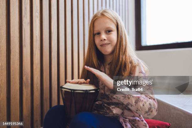 young girl smiling while playing a drum and holding it in her lap - slagverksinstrument bildbanksfoton och bilder