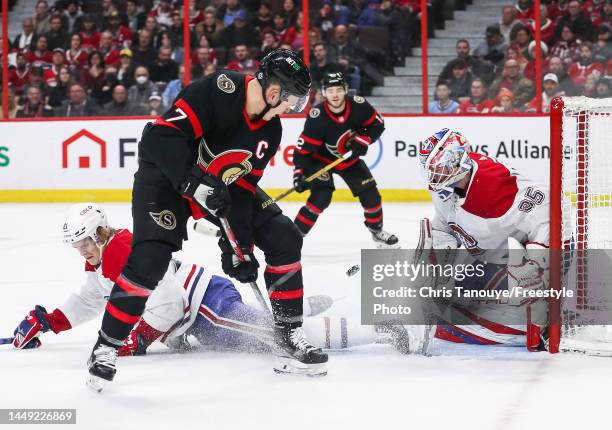 Brady Tkachuk of the Ottawa Senators shoots the puck between his legs as Kaiden Guhle of the Montreal Canadiens blocks the puck and his teammate Sam...