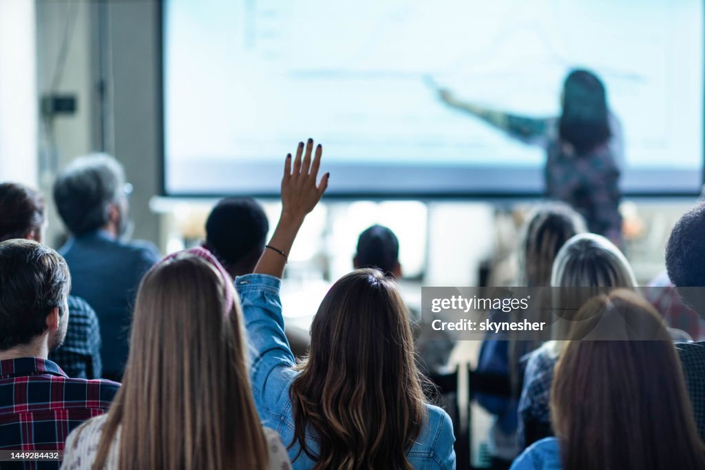 Back view of creative woman asking a question on education event in the office.
