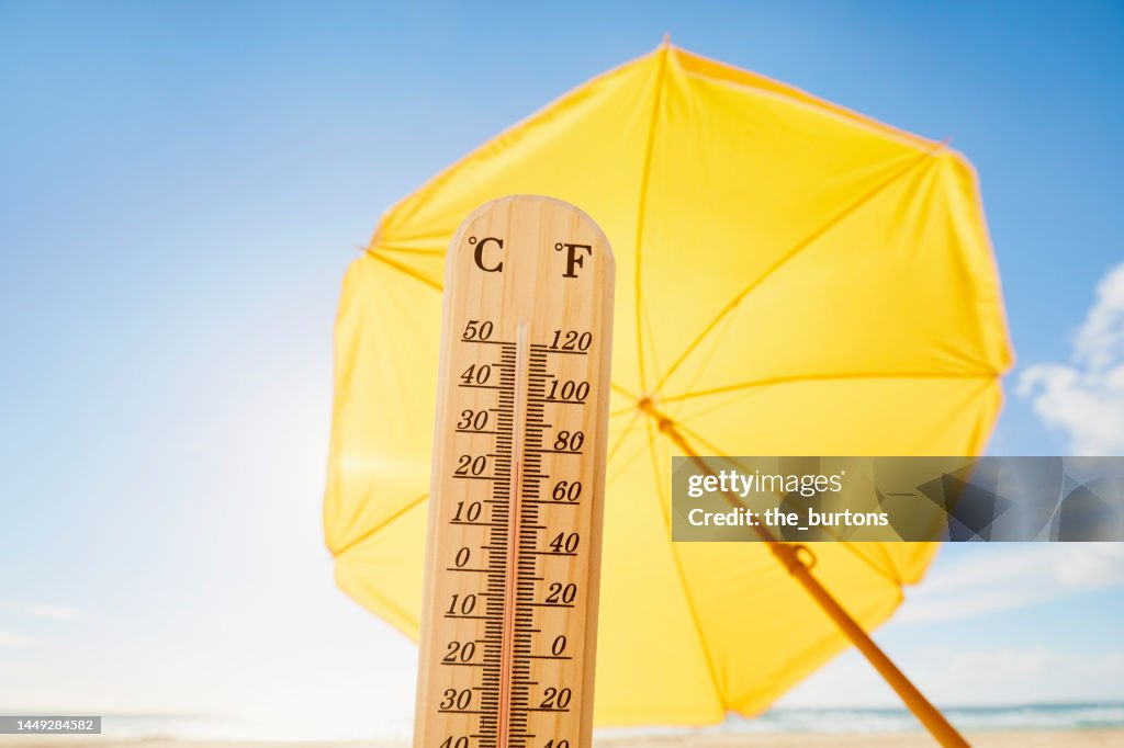 Thermometer at beach against yellow parasol