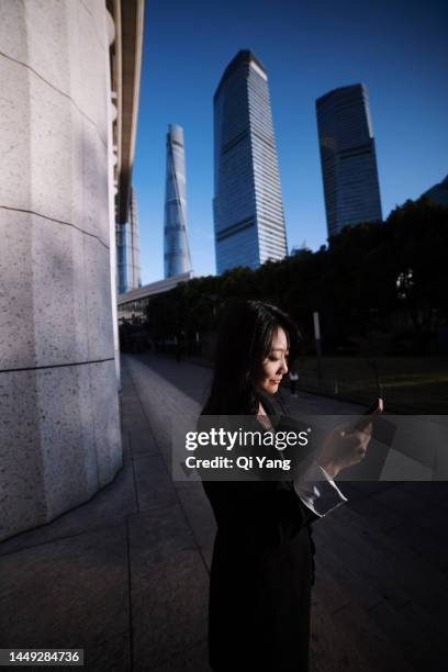 professional asian businesswoman using smartphone while standing in front of high-rise financial building in central business district of shanghai, china - people shanghai stockfoto's en -beelden