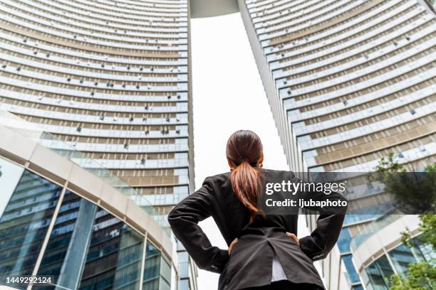 young business woman stands at enterance of skyscraper - expatriate stock pictures, royalty-free photos & images