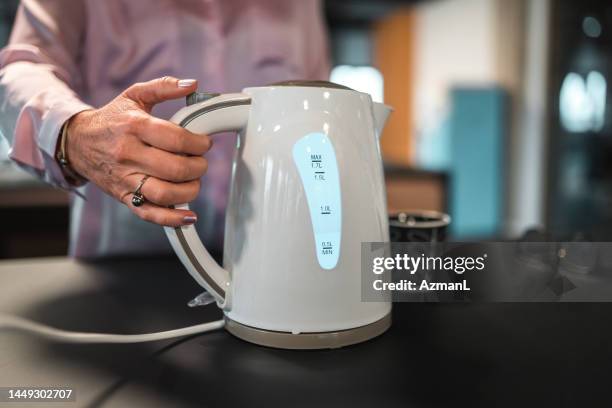 une employée de bureau de race blanche utilisant une bouilloire électrique au travail - bouilloire photos et images de collection