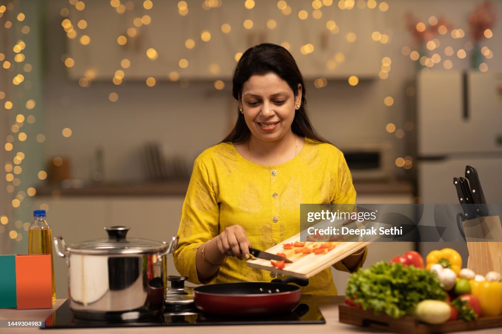 Portrait of Indian woman enjoying while cooking meal in the kitchen. stock photo