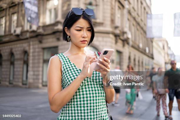 serious asian woman text messaging on smart phone in the city. - distraught stock pictures, royalty-free photos & images