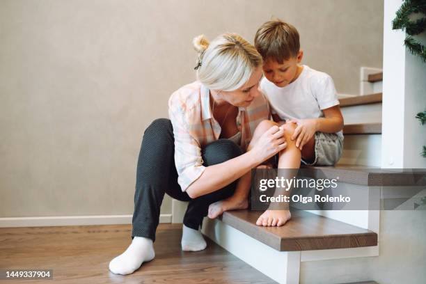 mother help and care for her son. mother curing, treating knee wound of little son - wunder stock-fotos und bilder