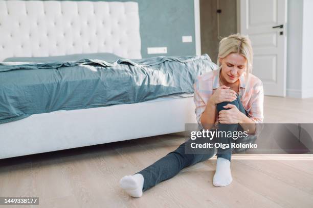 woman hugging her leg crossed at knee, sit near bed - rheuma stock-fotos und bilder