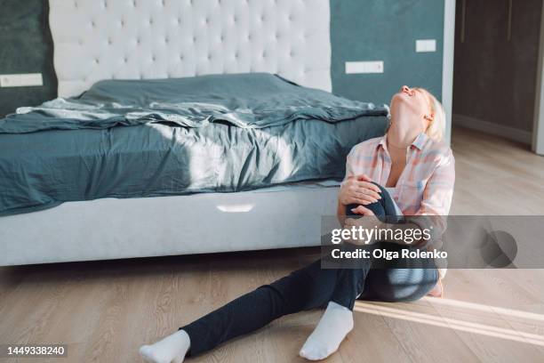 broken leg and bone bias. woman hugging her leg crossed at knee, with head turned away, sit near bed - calcita fotografías e imágenes de stock