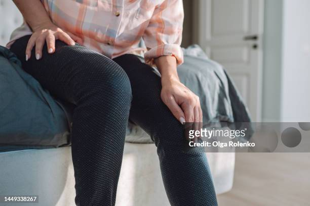 rheumatoid arthritis problem. close up of cropped woman hands touching and rubbing knees, sit on bed - artrite reumatoide - fotografias e filmes do acervo