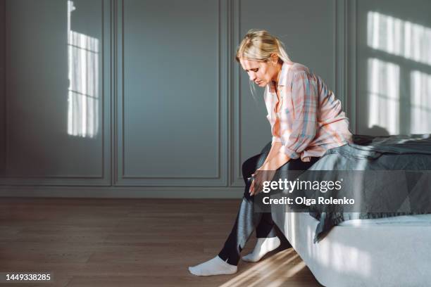 varicose pain and self massage. woman struggling from pain in legs, sit on bed - debolezza foto e immagini stock