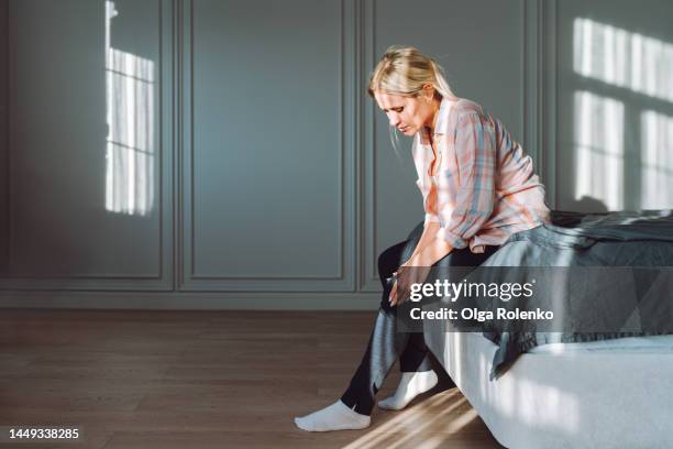 varicose pain and self massage. woman struggling from pain in legs, sit on bed - indecisive stockfoto's en -beelden