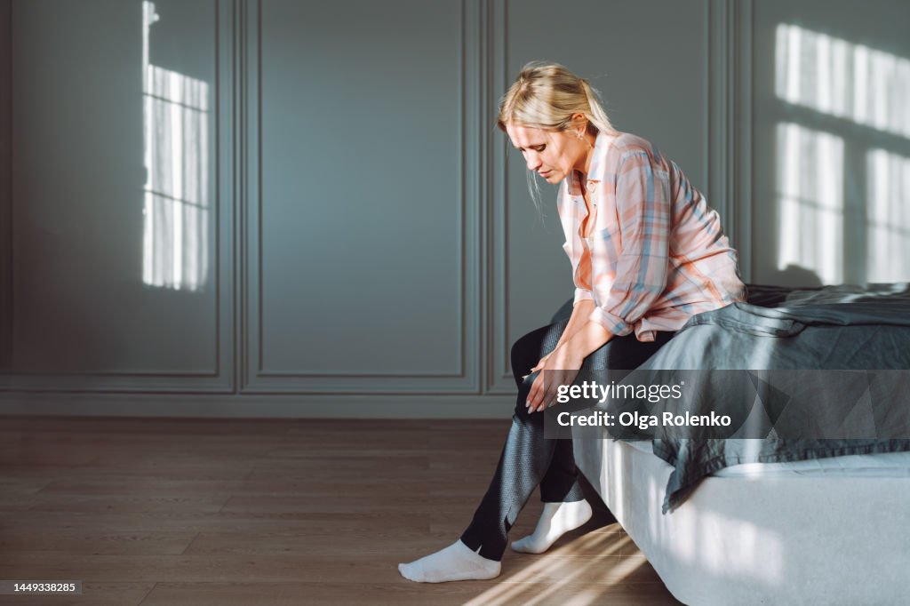 Varicose pain and self massage. Woman struggling from pain in legs, sit on bed
