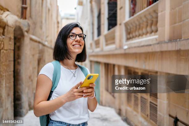 turista feminino jovem olhando para cima direções em um telefone inteligente em valletta - malta - fotografias e filmes do acervo