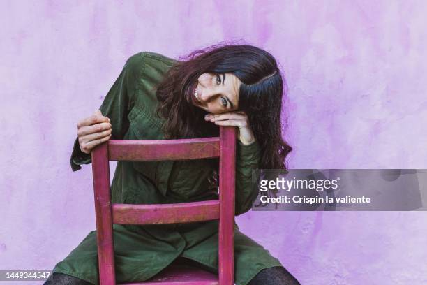 smiling brunette woman sitting on a chair in the studio, light purple background - beautiful woman 35 sit studio stock-fotos und bilder