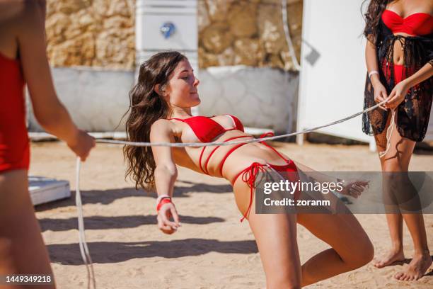 junge frau im roten bikini, die sich nach hinten beugt und tief unter dem limbo-seil geht - limbo stock-fotos und bilder