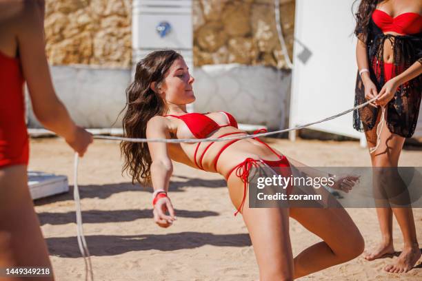 mujer joven en bikini rojo inclinándose hacia atrás y bajando bajo la cuerda del limbo - limbo fotografías e imágenes de stock